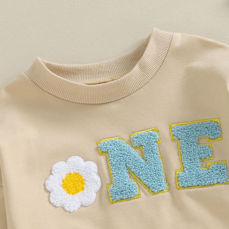 Beige sweatshirt with a white daisy and blue letters spelling 'ONE'.