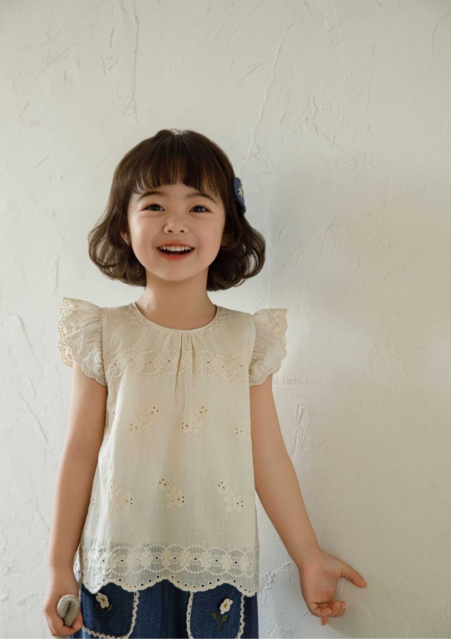 Beige sleeveless girls embroidered cotton top with floral embroidery and ruffle sleeves.